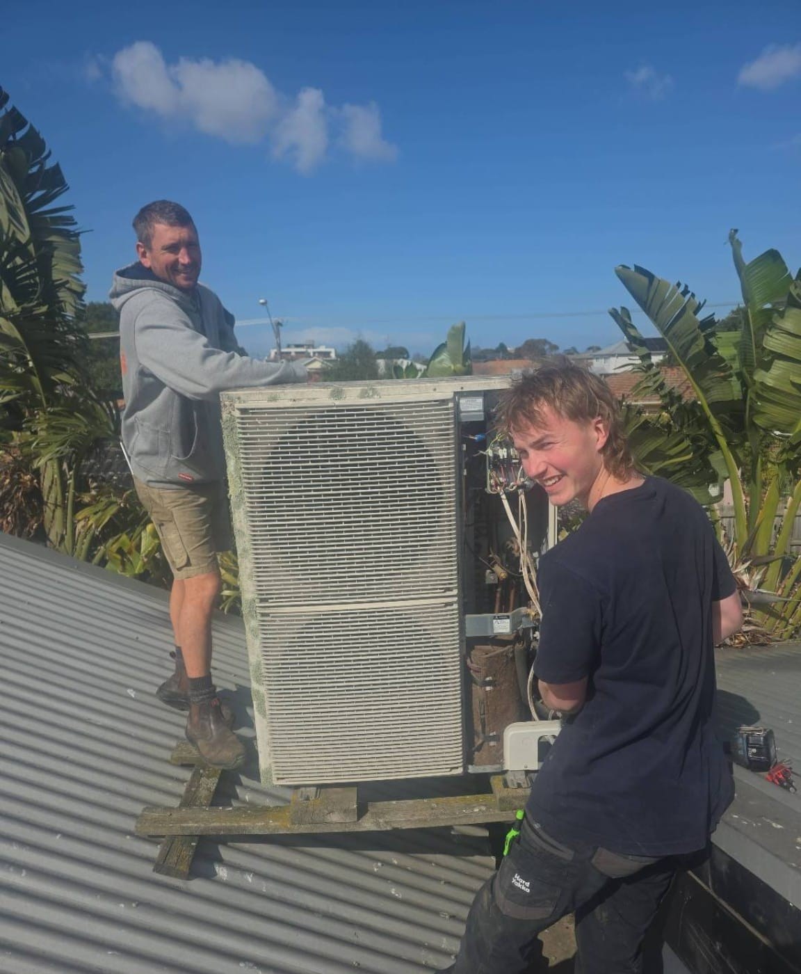 Jesse and his apprentice on a tin roof with a large outdoor unit